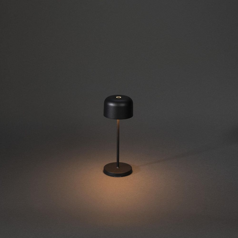 Eine kleine schwarze Tischlampe mit rundem Sockel und Schirm steht auf einem dunklen Hintergrund.