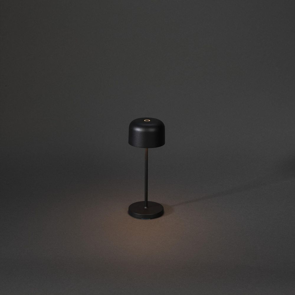 Eine schwarze Tischlampe mit rundem Fuß und Lampenschirm steht auf dunklem Grund.