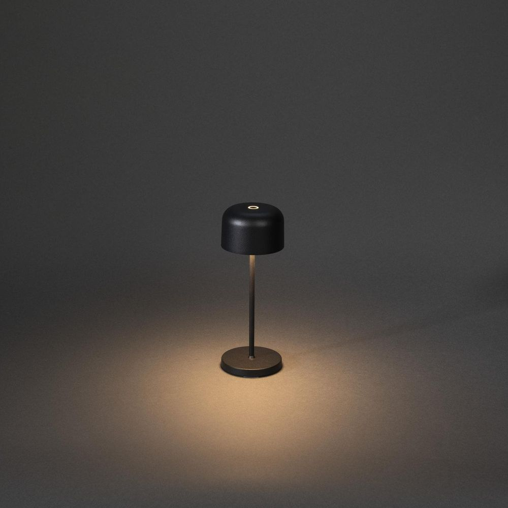 Schwarze Tischlampe mit rundem Fuß auf dunklem Hintergrund, beleuchtet von unten.