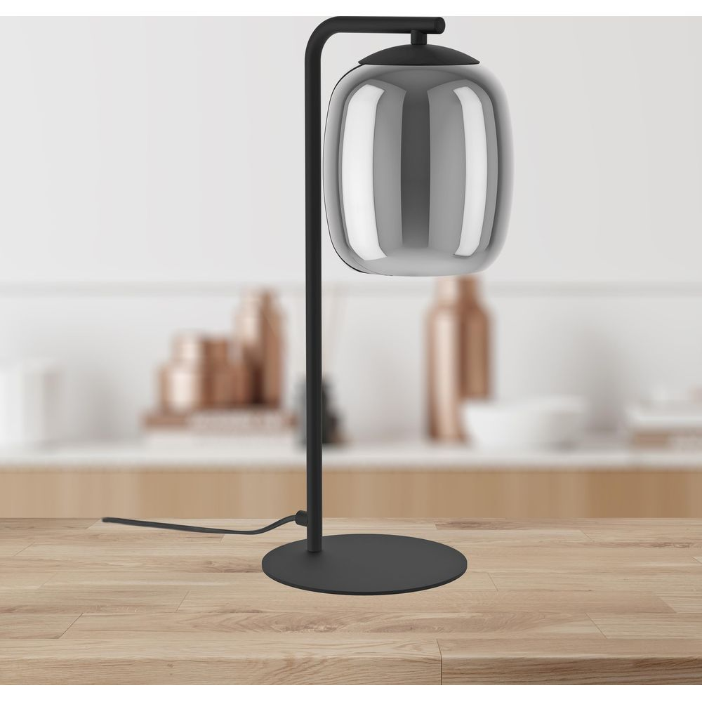 Eine schwarze Tischlampe mit einem spiegelnden, ovalen Lampenschirm steht auf einem Holztisch.