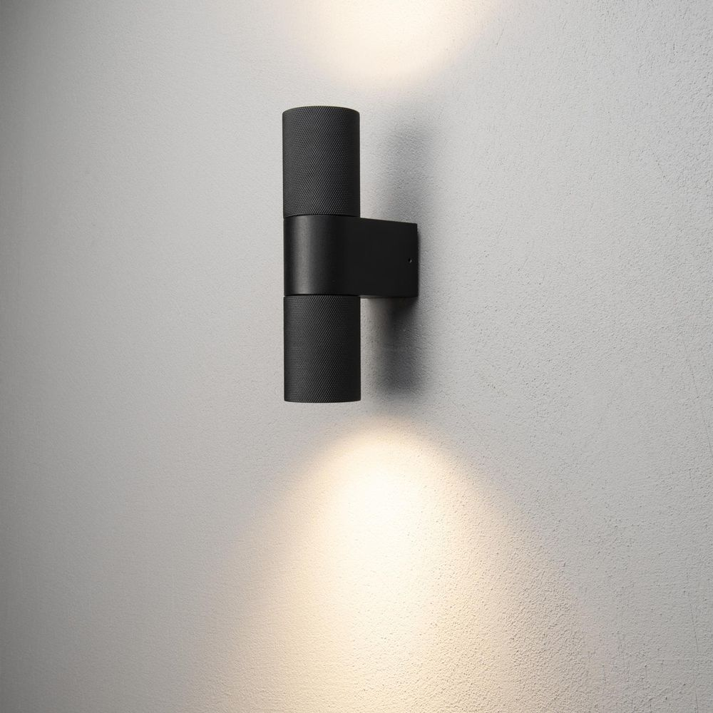 Eine schwarze Wandleuchte mit zwei zylindrischen Lampenschirmen sendet Licht nach oben und unten.