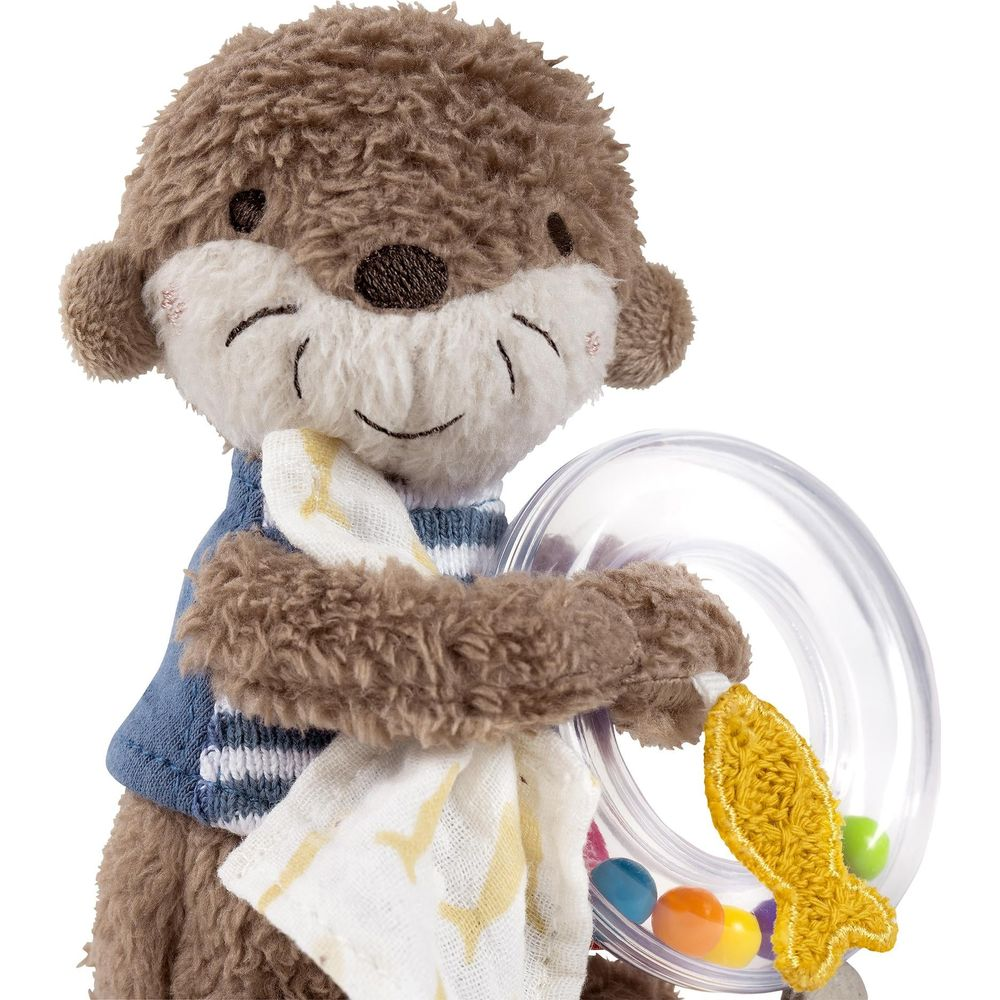 Une loutre en peluche avec un pull bleu et blanc rayé tient un hochet avec des billes colorées.