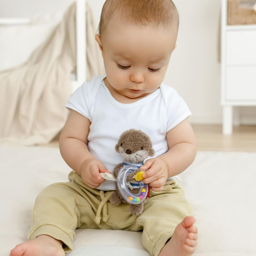 Bébé assis par terre jouant avec une peluche et un hochet.