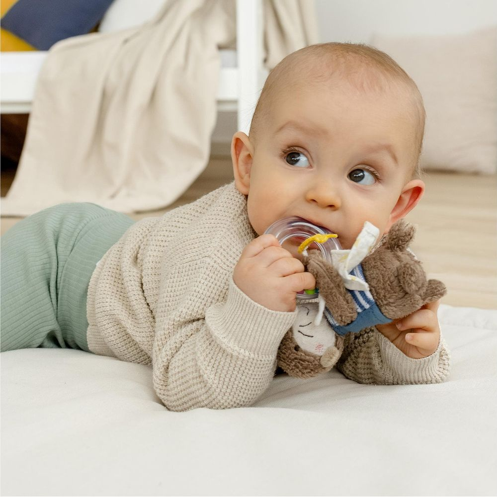 Bébé allongé sur le ventre, mâchant un hochet ours en peluche avec anneau de dentition.