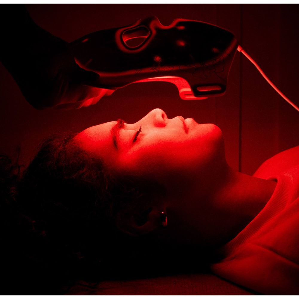 Kobieta leży z zamkniętymi oczami pod czerwonym światłem urządzenia.