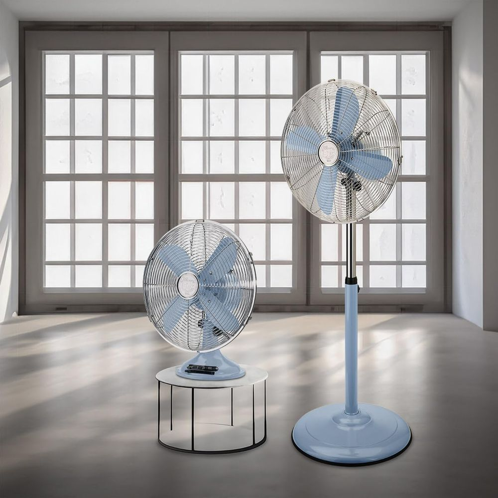 Due ventilatori blu davanti a una finestra con griglie. Uno è su un tavolino, l'altro su un piedistallo.