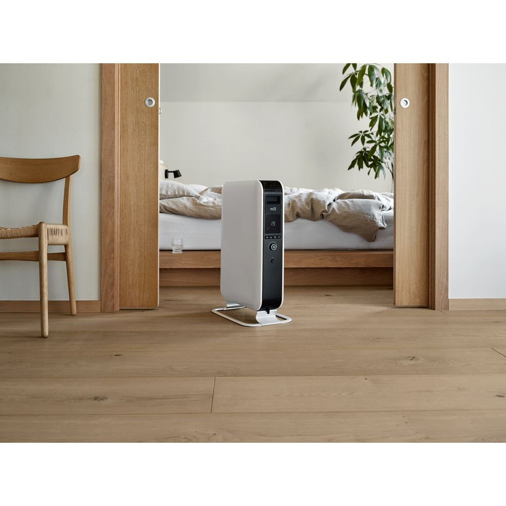 Ein weißer Heizkörper steht auf einem Holzboden neben einem Bett.