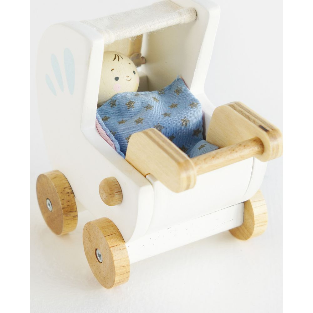 Biała, drewniana zabawka wózek dla lalek z materiałową lalką przykrytą niebieskim kocykiem w gwiazdki.