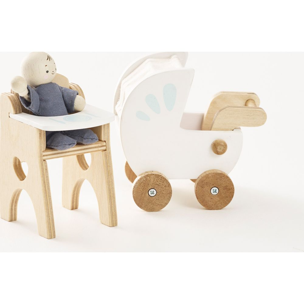 Drewniana lalka w krzesełku do karmienia obok białego wózka zabawkowej z drewnianymi kołami.