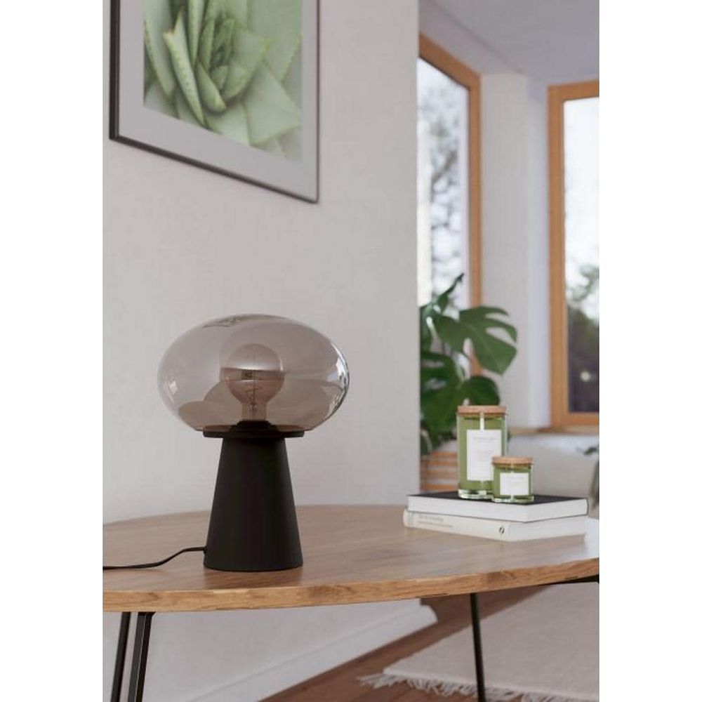 Ein schwarzer Tisch mit einer Lampe, Büchern und Kerzen, daneben ein Fenster.