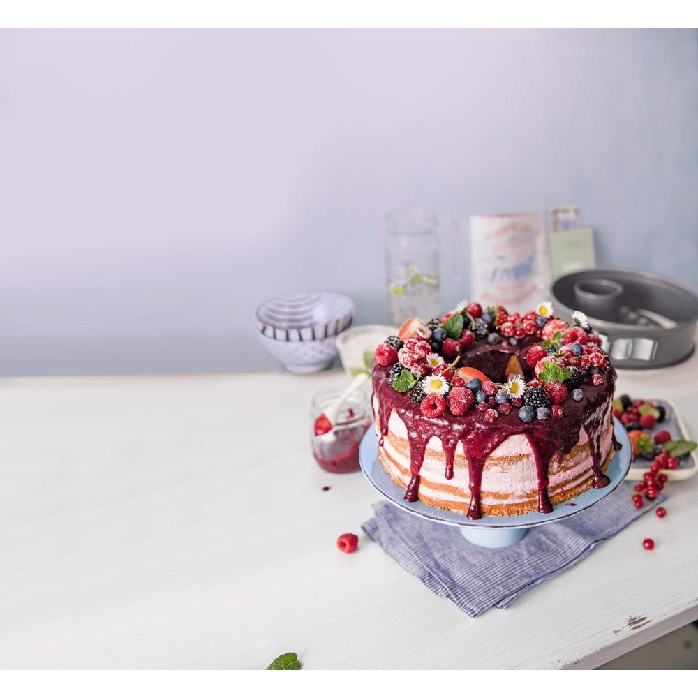 Okrągły tort z jagodami i polewą czekoladową na stojaku.