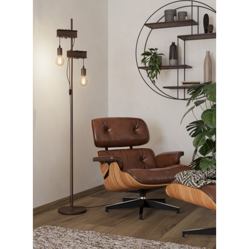 Ein brauner Ledersessel mit Ottomane steht neben einer Stehlampe mit zwei Glühbirnen.