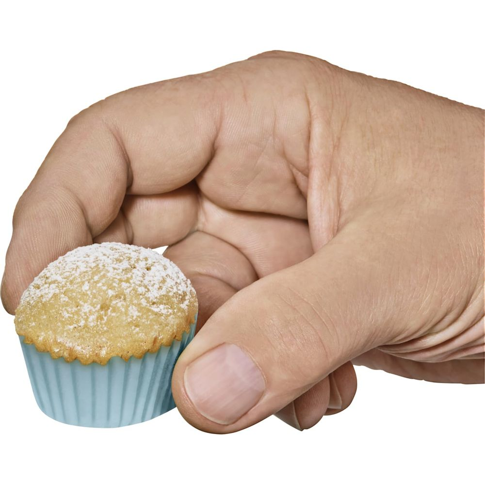 Eine Hand hält einen kleinen, mit Puderzucker bestreuten Muffin in einer blauen Form.