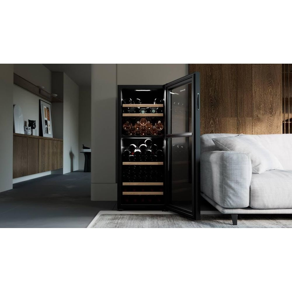 Ein offener Weinkühlschrank mit vielen Flaschen daneben ein Sofa.