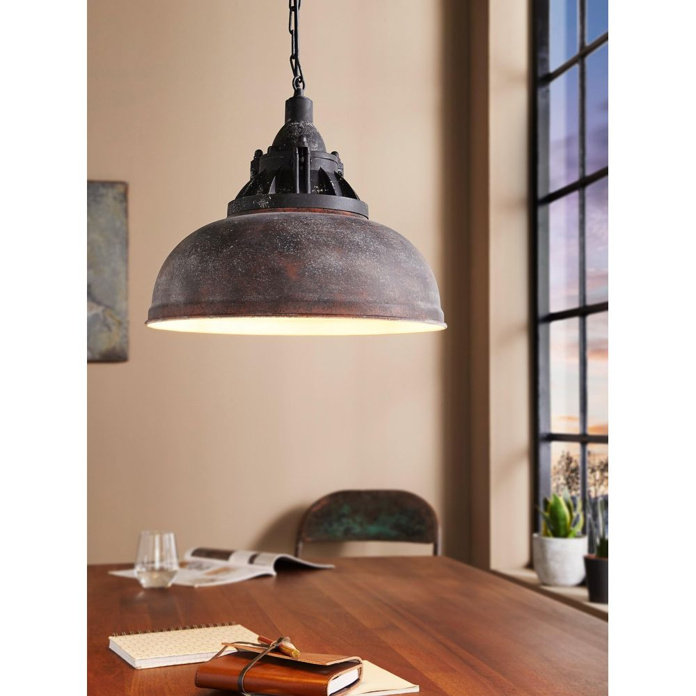 Lampada a sospensione industriale su tavolo in legno con taccuino e bicchiere.