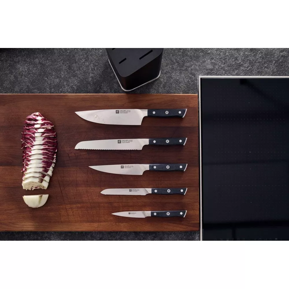 Pięć noży i cykoria na desce drewnianej obok płyty grzewczej.