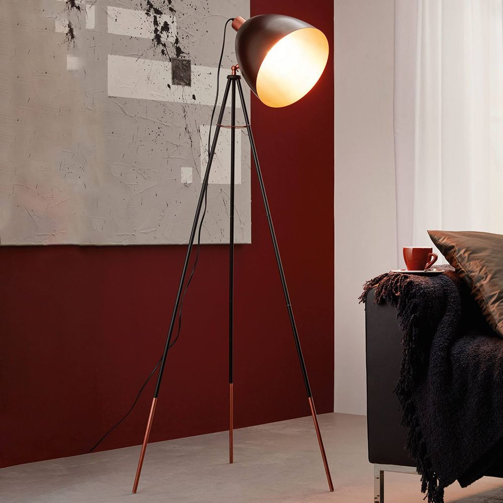 Una lampada da terra a treppiede illumina una stanza con muro rosso e arte.