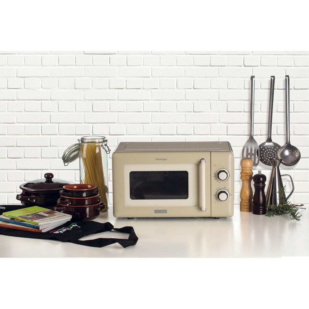 Kremowy piekarnik mikrofalowy na białej powierzchni przed ceglanym murem.