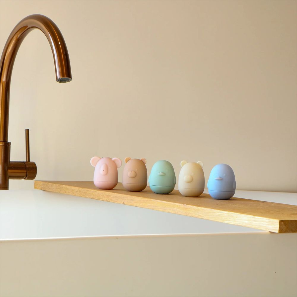 Fünf bunte Tierfiguren stehen nebeneinander auf einem Holzbrett neben einem Wasserhahn.