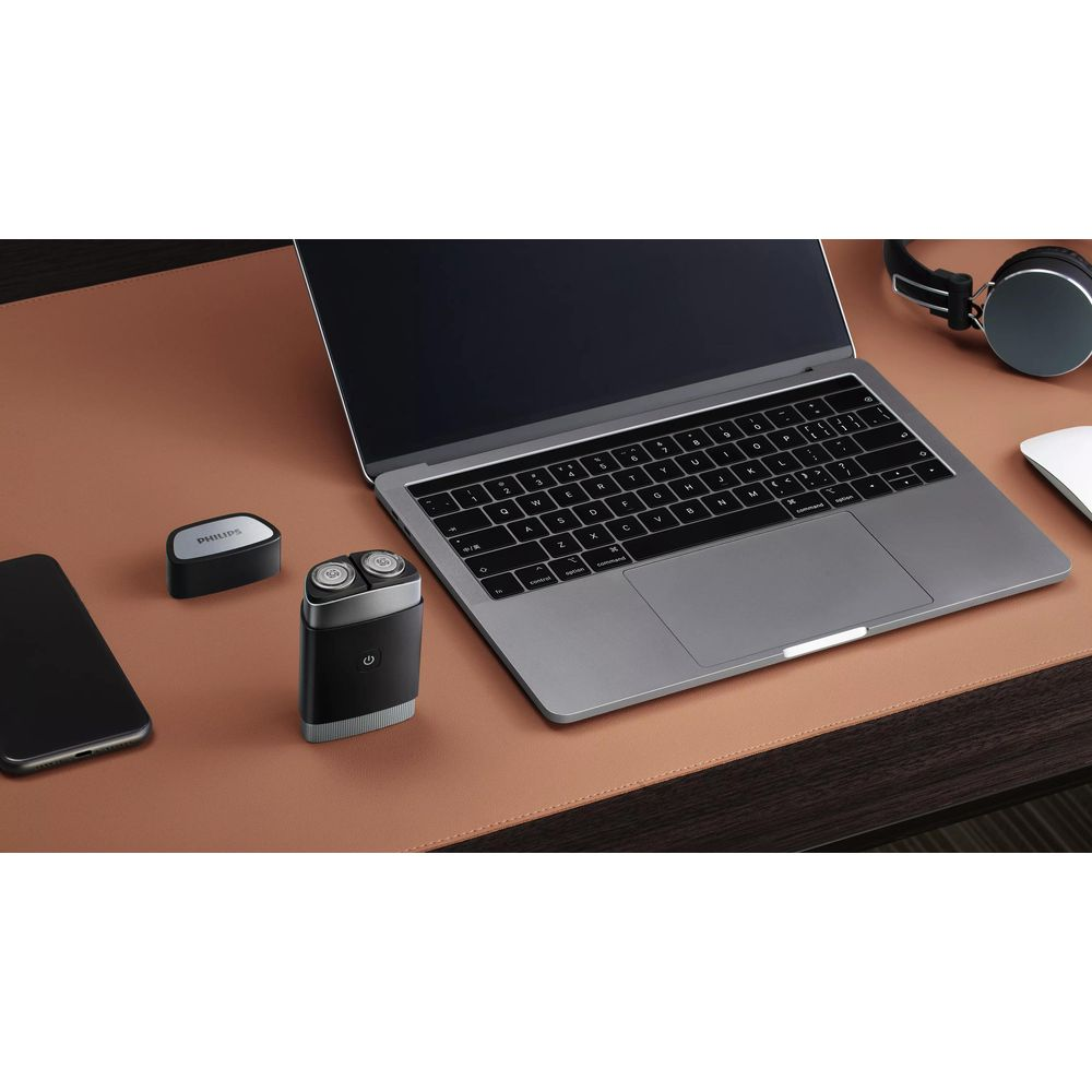 Laptop, telefon, golarka, mysz i słuchawki na brązowej podkładce na biurko.