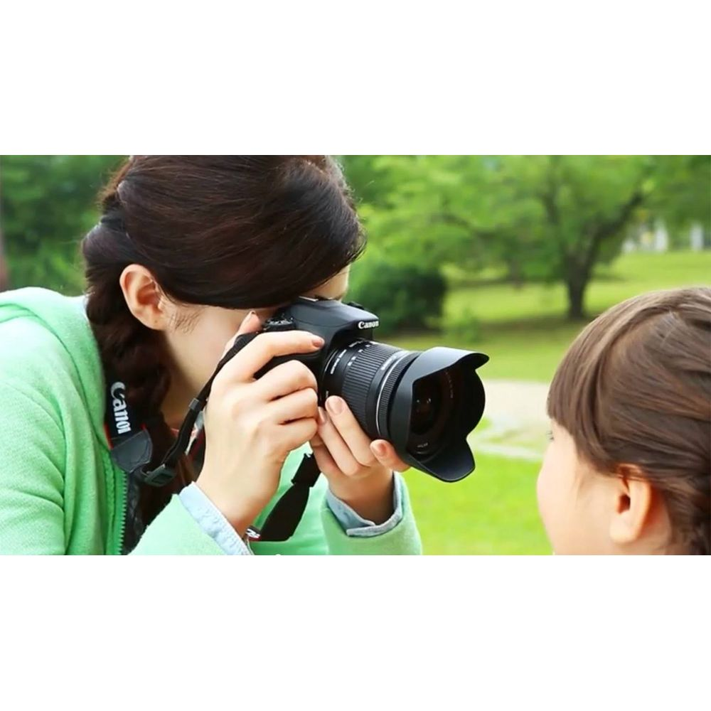 Frau fotografiert Kind mit Kamera im Freien mit Bäumen im Hintergrund.