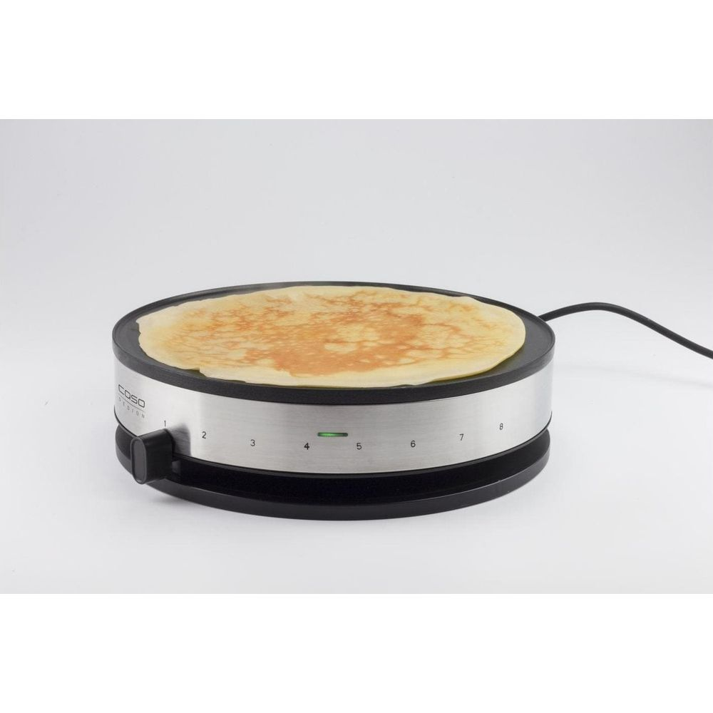 Een crêpemaker met een goudbruine crêpe op het zwarte kookoppervlak, vanuit een licht verhoogde hoek getoond.