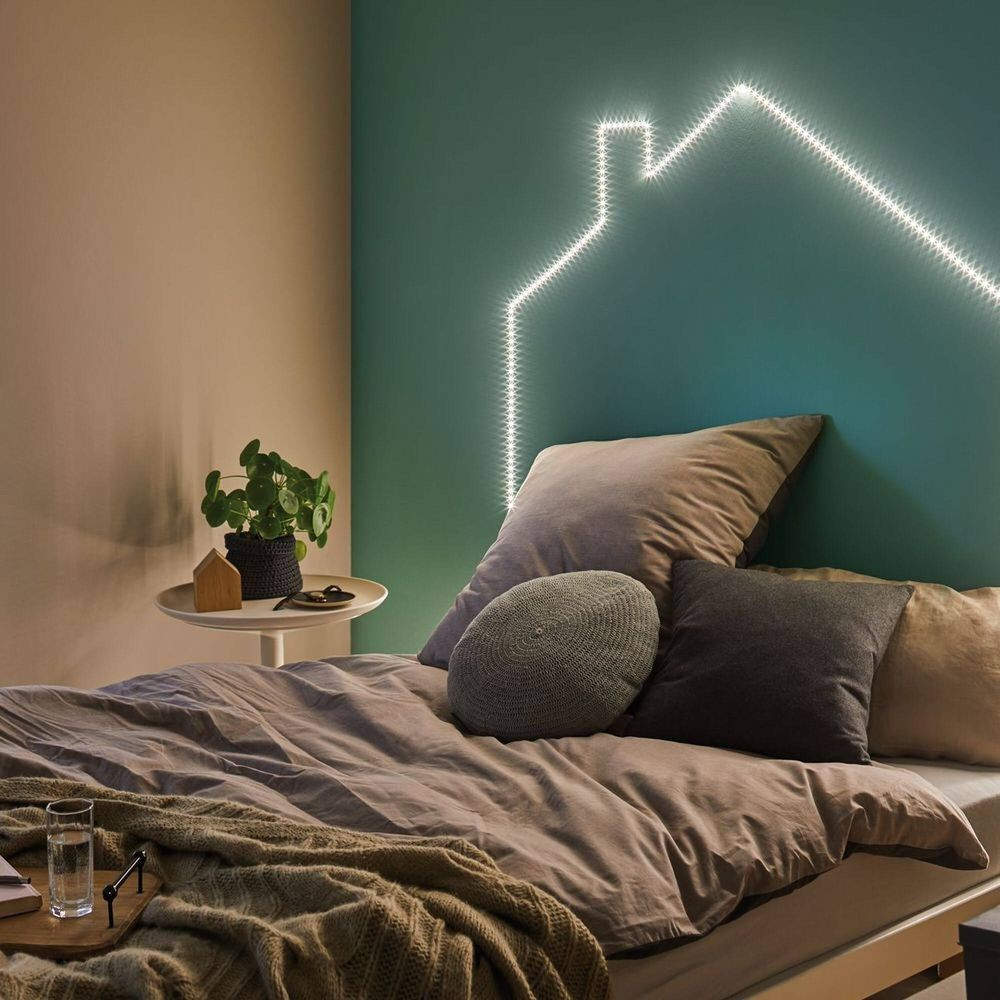 Ein Bett mit Kissen und einer Haus-förmigen Lichterkette an der Wand.