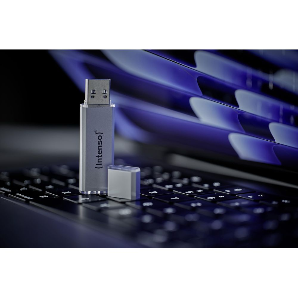 Een zilveren USB-stick met dop op een toetsenbord, laptop op achtergrond.