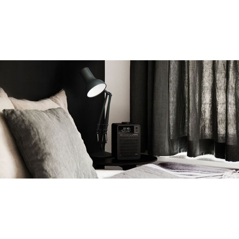 A bedside table with a lamp and radio next to a bed with pillows.