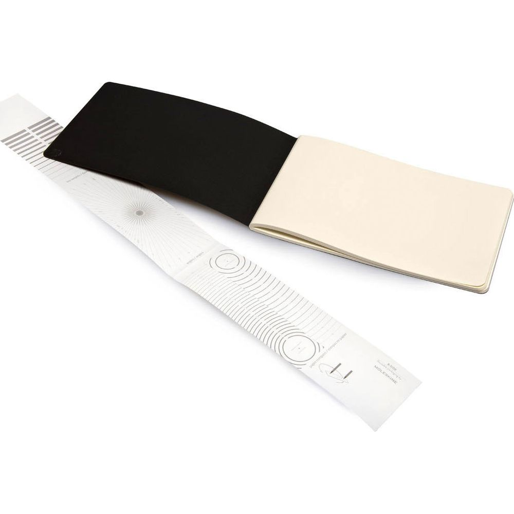 Otwarty notatnik z czarną okładką i kremowymi stronami leży obok złożonego arkusza papieru z grafiką.