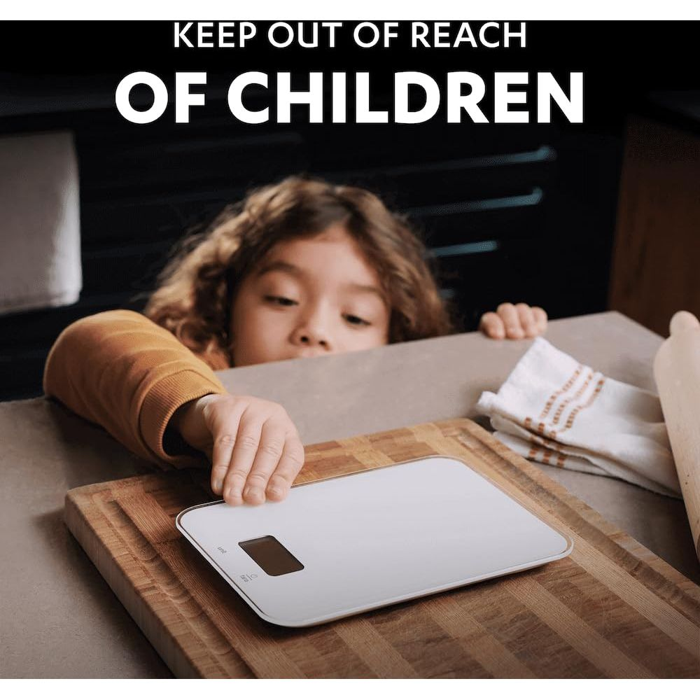 Dziecko sięga po wagę cyfrową na drewnianym blacie. Tekst: Przechowywać z dala od dzieci.