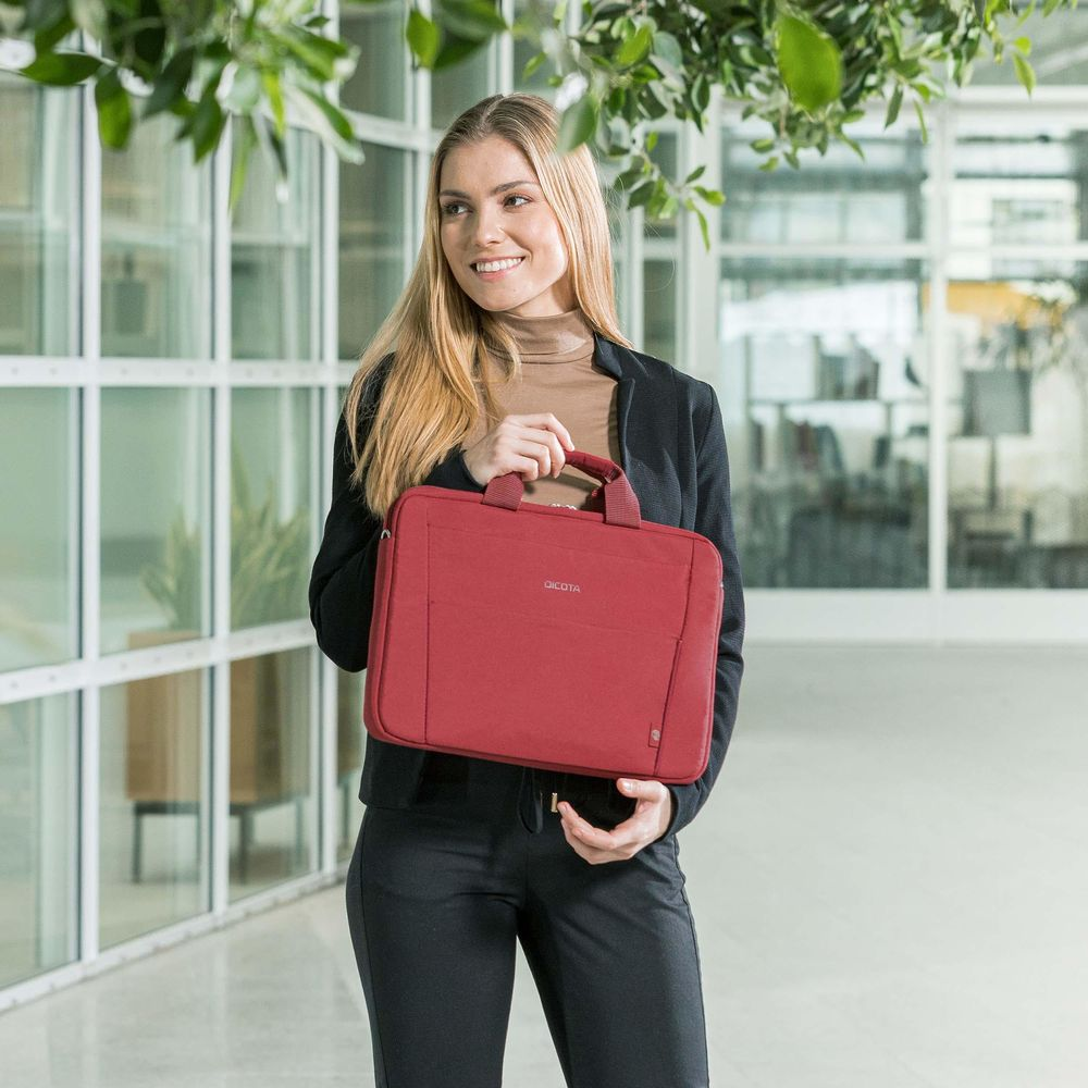 Eine Frau mit langen blonden Haaren hält eine rote Laptoptasche in einem modernen Büro.