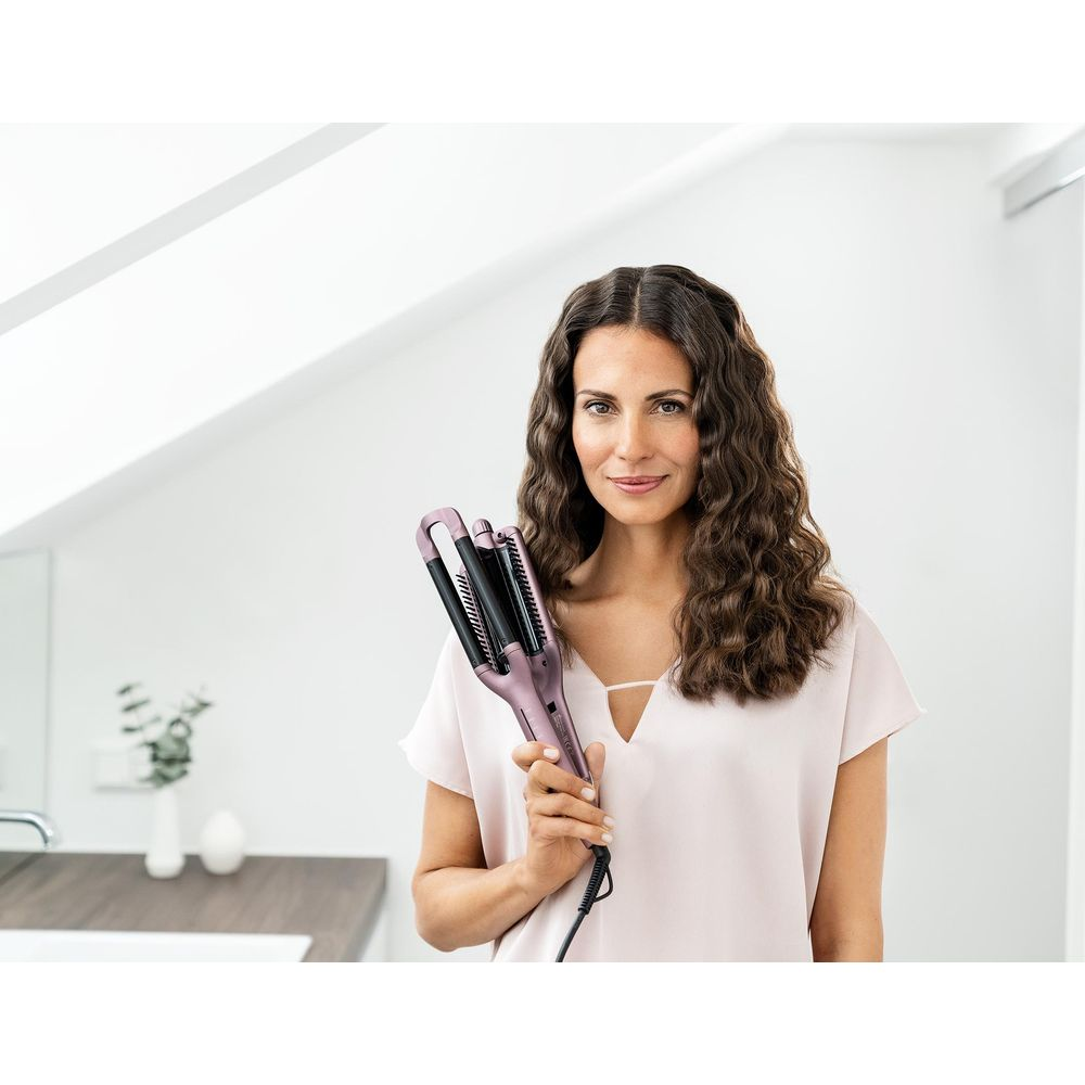 Eine Frau hält einen rosafarbenen Haarglätter mit mehreren Lockenstäben.