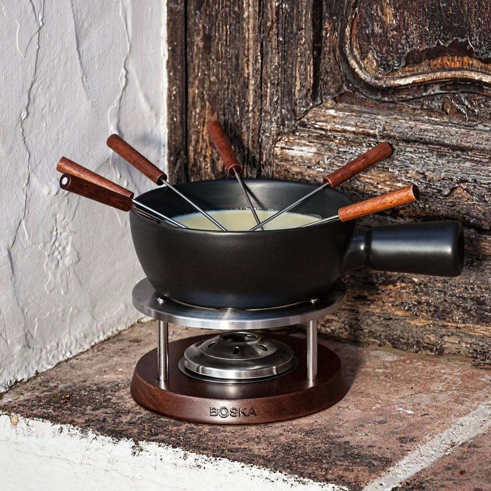 A black fondue pot with wooden handles sits on a wooden stand over a heat source.