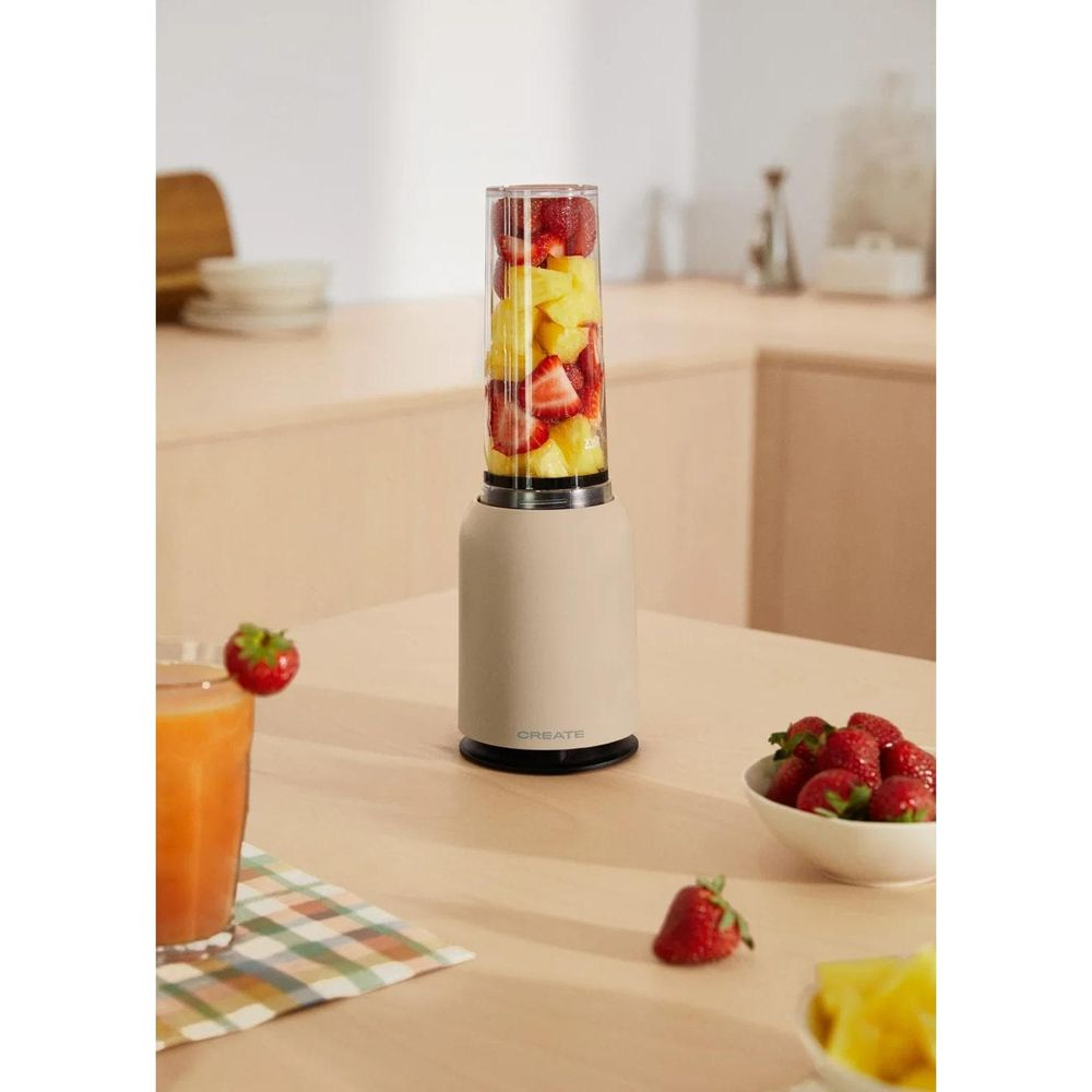 Ein Mixer mit Erdbeeren und Ananas gefüllt steht auf einem Tisch neben einem Glas Saft.