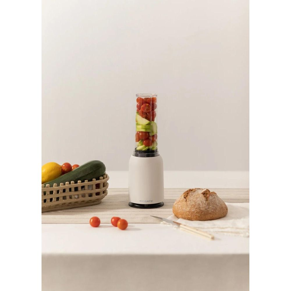 Ein Mixer mit Tomaten und Gurken, daneben ein Brot und ein Korb mit Gemüse.
