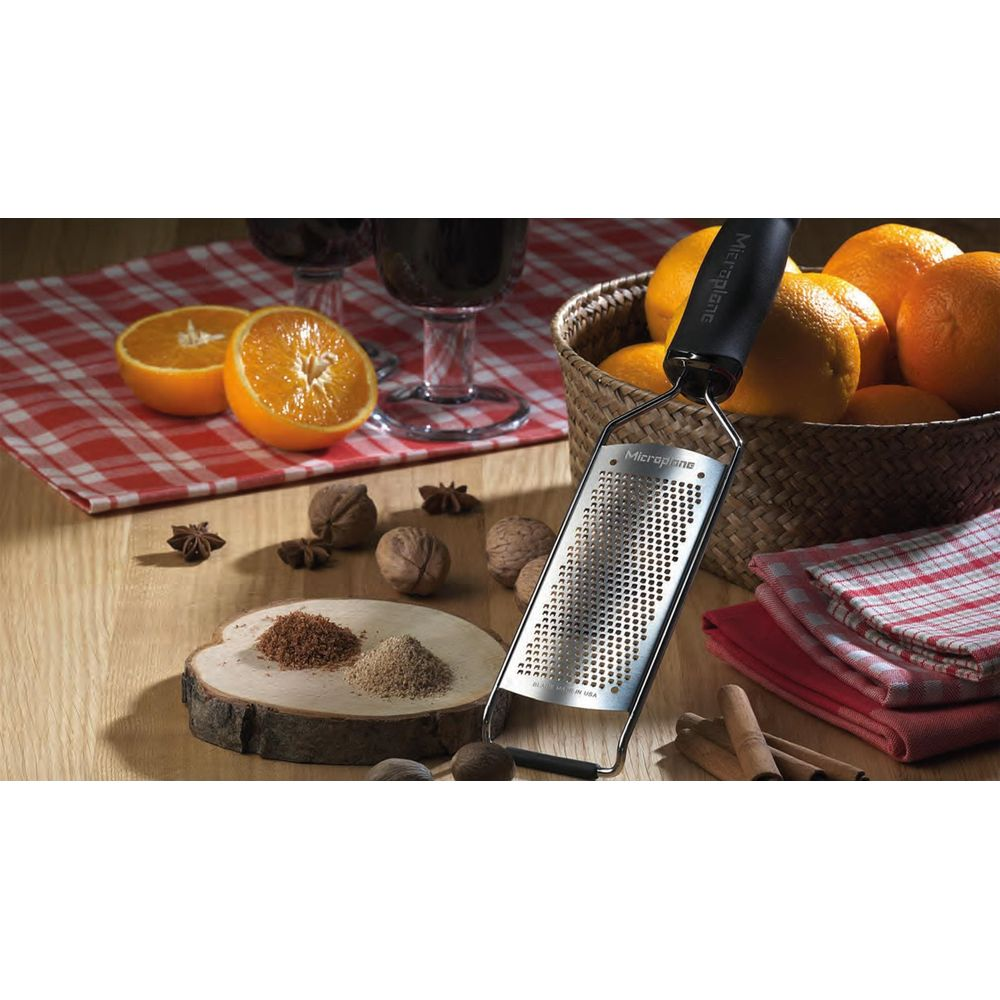 Zitrusfrüchte, Nüsse, Gewürze und ein Reibeisen auf einem Holztisch.