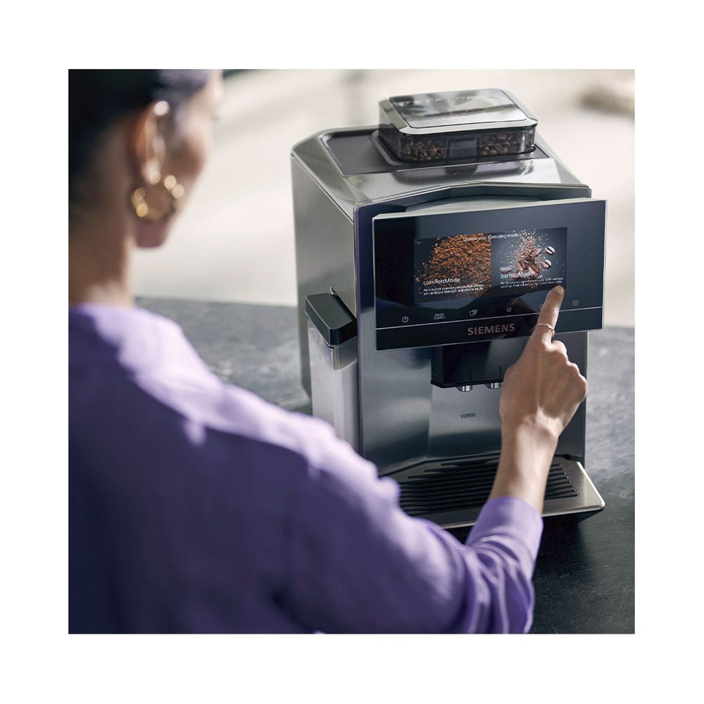 Kobieta w fioletowej bluzce obsługuje ekspres do kawy z ekranem dotykowym.