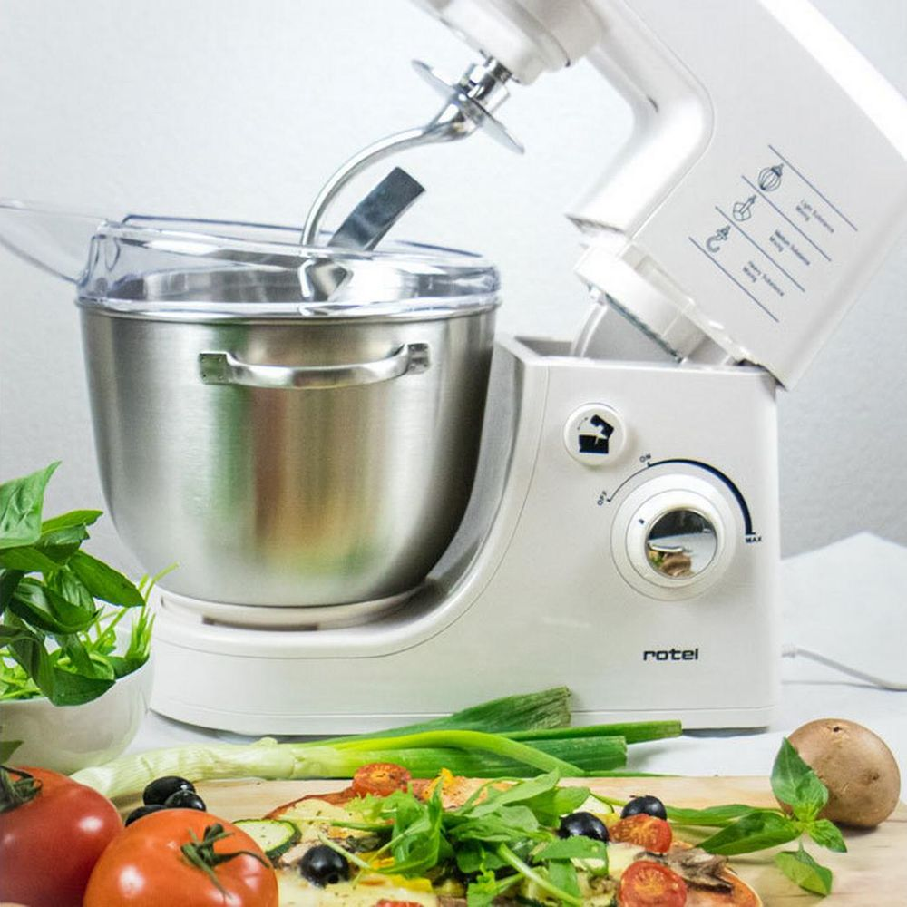 Un robot pâtissier blanc avec bol en inox, à côté d'une pizza et d'ingrédients.