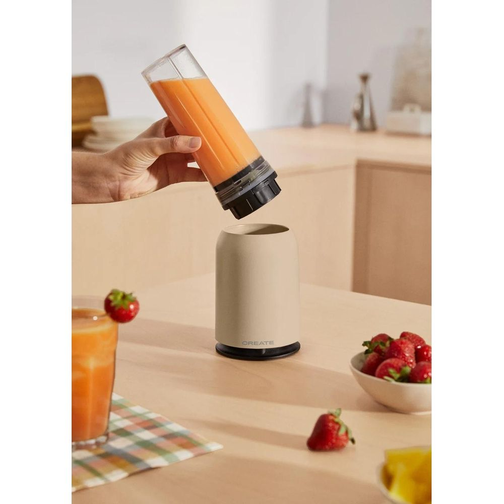 Eine Hand hält einen Mixerbecher mit Orangensaft über einen beigefarbenen Sockel.