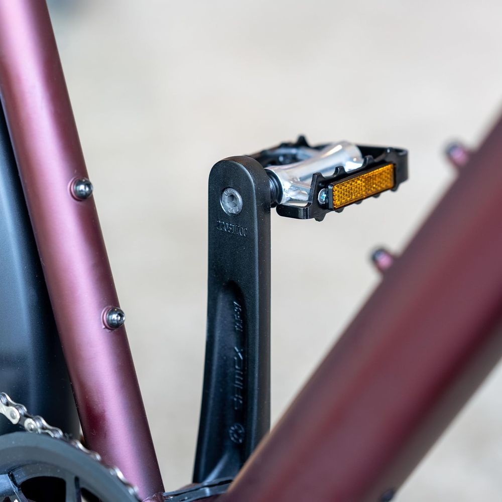 Zbliżenie pedału rowerowego ze srebrnymi detalami i odblaskami na czarnym ramieniu korby.