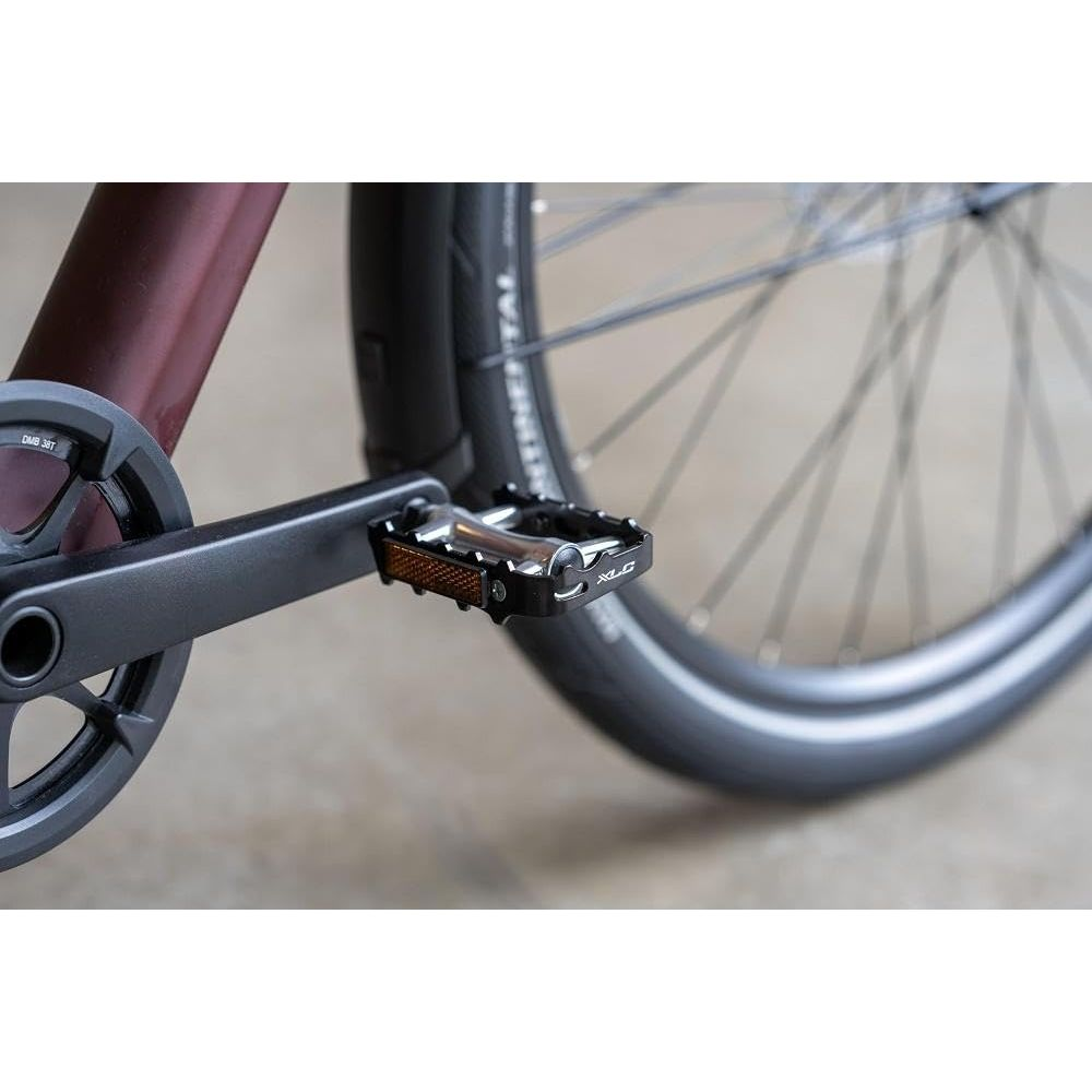 Zbliżenie na pedał i korbę roweru, z częściowym kołem w tle.