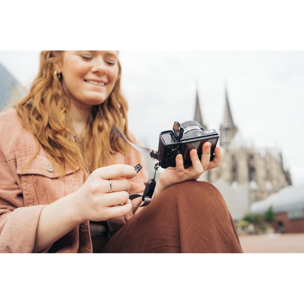 Rudowłosa kobieta trzyma aparat i kartę pamięci przed katedrą.