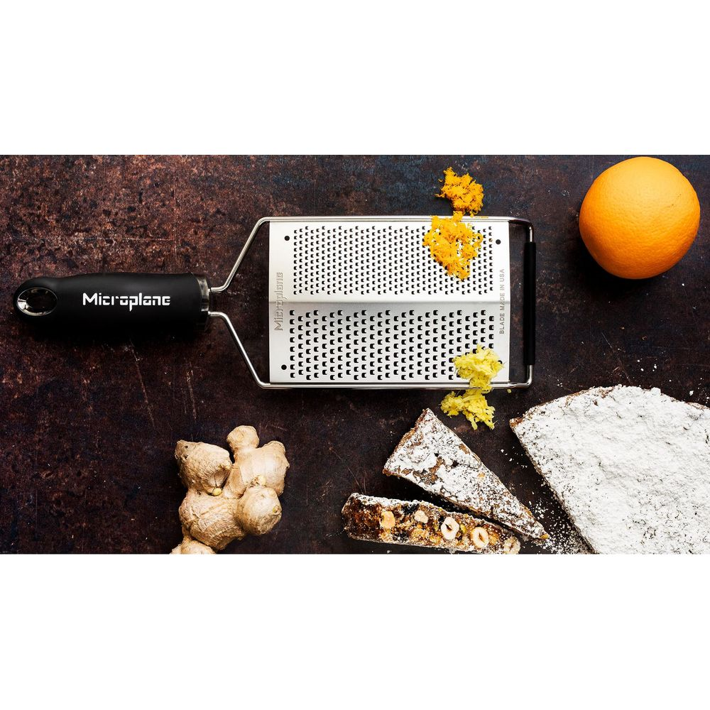 Eine Microplane-Reibe mit Orangenzesten, Ingwer, einer Orange und Panforte auf dunkler Oberfläche.