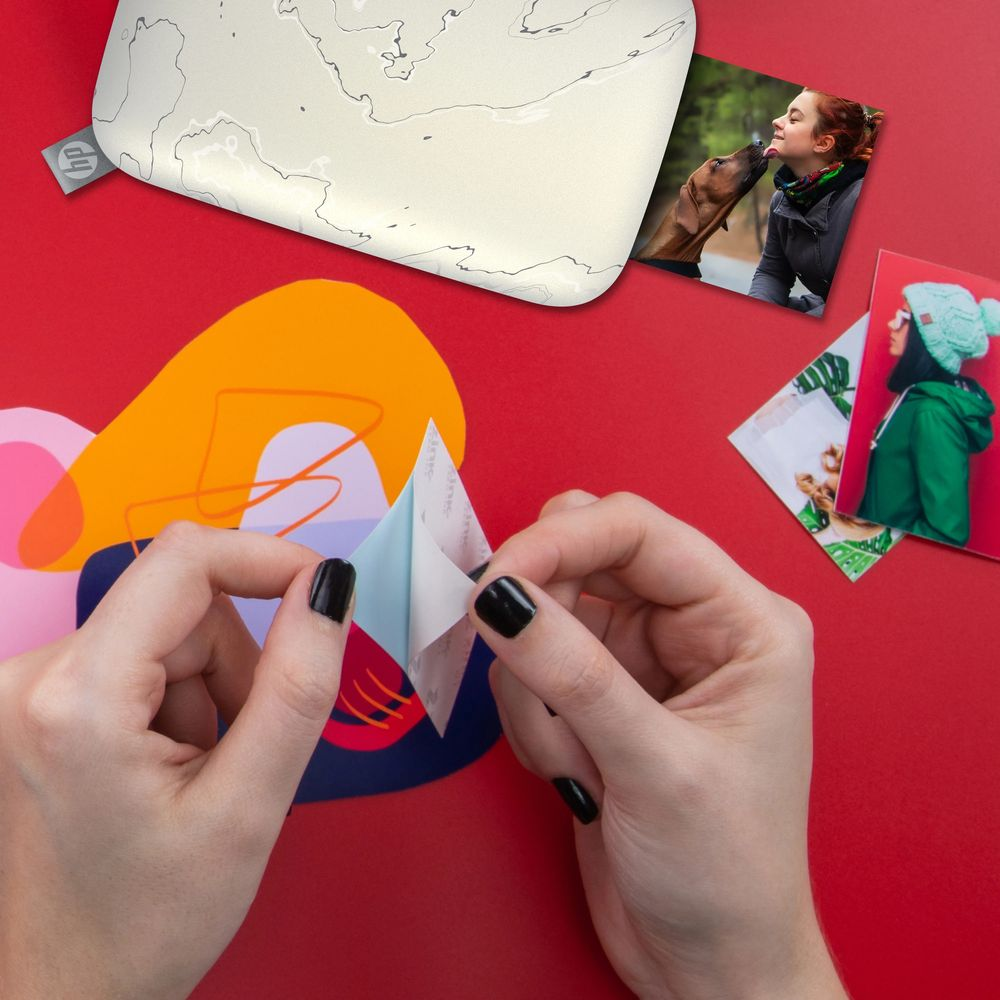 Ręce odklejają naklejkę ze zdjęcia. Pies liże kobietę. Czerwone tło.