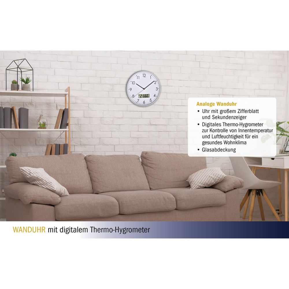 Analoge Wanduhr mit digitalem Thermo-Hygrometer auf Backsteinwand über Sofa.