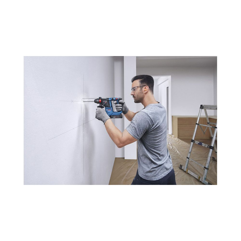 Mann bohrt in weiße Wand mit blauer Bohrmaschine. Leiter im Hintergrund.