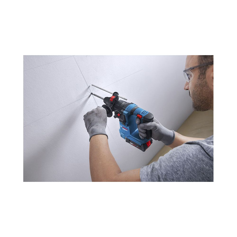 Mann bohrt mit blauem Bohrhammer in weiße Wand. Graue Handschuhe.