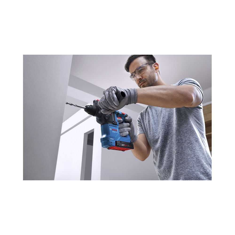 Mann bohrt mit blauem Bohrhammer in weiße Wand, trägt Schutzbrille und Handschuhe.