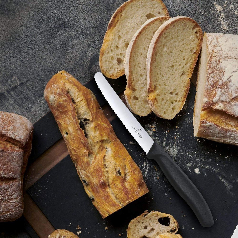Ein Brotmesser liegt auf einem schwarzen Brett neben verschiedenen Brotsorten.